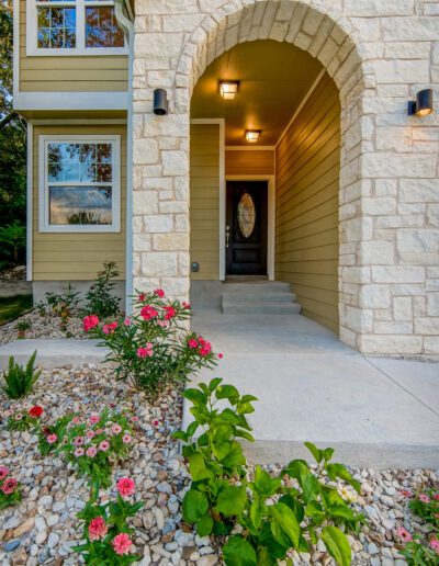 Front entrance of a modern house with an arched doorway, stone facade, and a landscaped garden.